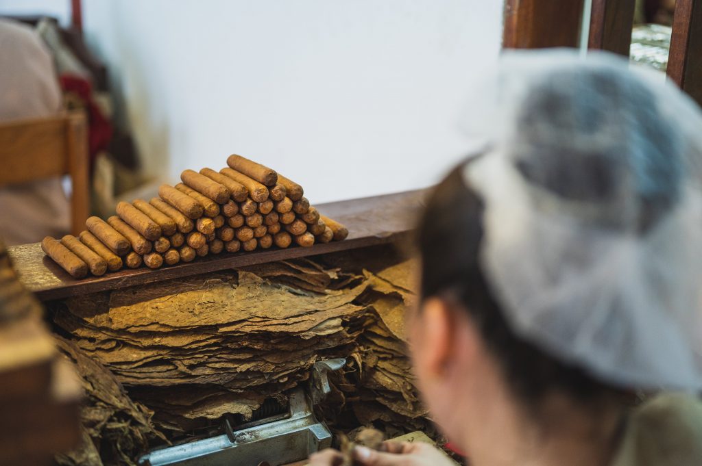 https://www.pexels.com/id-id/foto/pekerja-tak-berwajah-mengupas-daun-tembakau-di-dekat-tumpukan-sosis-di-pabrik-3975064/