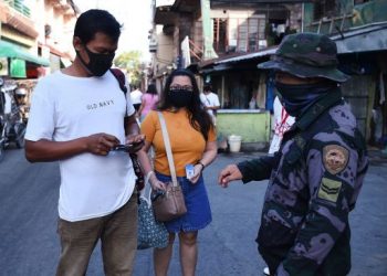 Anggota polisi memeriksa identifikasi karantina yang diperlukan dari penduduk di Navotas, pinggiran kota Manila, Filipina, Kamis (16/7). [Ted ALJIBE / AFP]