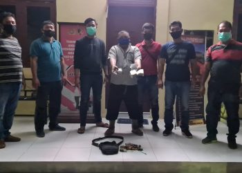 Foto tersangka diapit petugas sambil memperlihatkan barang bukti.