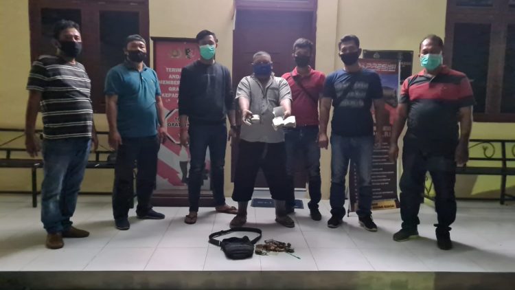 Foto tersangka diapit petugas sambil memperlihatkan barang bukti.