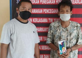 Foto pelaku memegang barang bukti ponsel.
