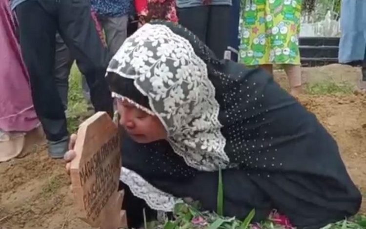 Bonia, istri wartawan korban penembakan OTK di Simalungun meratapi nisan suaminya. (Foto : iNews/Dharma Setiawan)