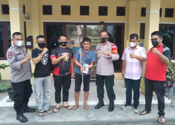 Pelaku pencurian diapit petugas sambil memegang barang bukti.