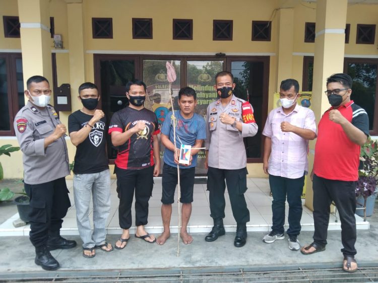 Pelaku pencurian diapit petugas sambil memegang barang bukti.