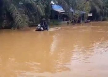 Seorang pengendara motor mendorong kendaraanya yang mogok akibat banjir di Madina. (Foto: iNews/Ahmad Husein Lubis).