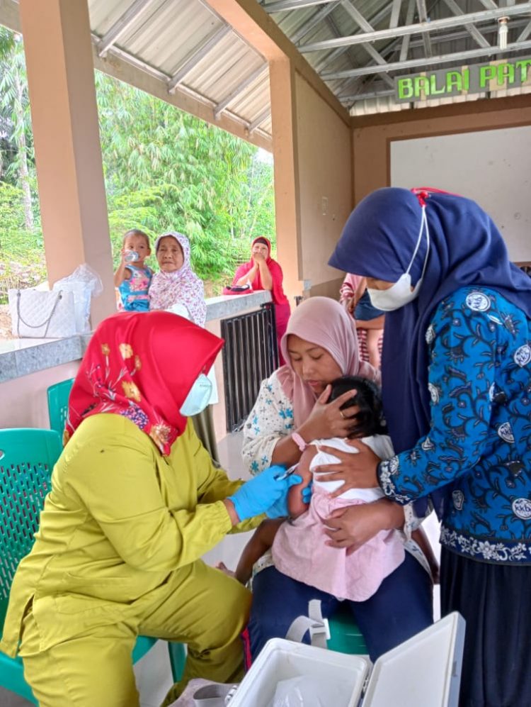 Ketua Tim Penggerak PKK Nagori Bukit Rejo, Uci Damanik (kanan) mendampingi Bidan Desa Nagori Bukit Rejo, Sri Murba, Am.Keb, saat memberikan imunisasi pada anak.