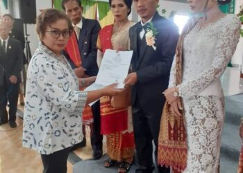Pegawai Dinas Dukcapil Humbahas, Naudur Purba SE saat serahkan akta perkawinan kepada pengantin pasangan baru, Rinto Lumbanbatu dengan Ivo Septi Maria Parhusip, Kamis (20/7/2023) lalu, di HKBP Pintubosi Ressort Onanganjang.