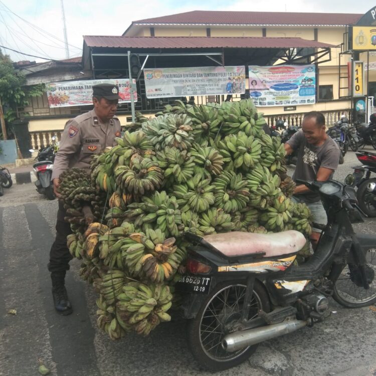 Bhabinkamtibmas Kelurahan Bantan, AIPDA Rayendra P. Damanik, gerak cepat bantu seorang warga angkat buah pisang yang jatuh dari kendaraannya.