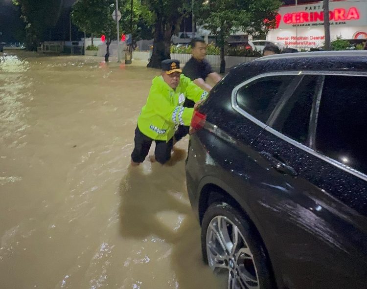 Kapolda Sumut, Irjen Pol Whisnu Hermawan Februanto, ikut mendorong mobil yang mogok akibat genangan banjir di Jalan Jenderal Sudirman, Medan, Kamis (27/11). Aksi ini menunjukkan kepedulian langsung Kapolda terhadap warga dan upaya menjaga kelancaran arus lalu lintas.
