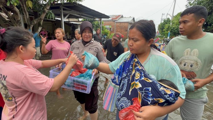 Aiptu Susi Pane bersama personel Polsek Medan Tembung dan SPPG Bhayangkari Polrestabes Medan berjalan di genangan banjir dengan celana digulung dan tanpa alas kaki saat membagikan makanan kepada warga di Desa Sampali, Kecamatan Percut Sei Tuan. Terlihat seorang ibu menggendong bayinya menerima bantuan tersebut di tengah banjir yang melanda wilayah setempat, Jumat (28/11/2025).