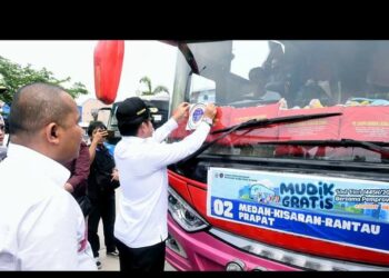 Pj Gubernur Sumut, Hasanuddin menempelkan stiker mudik gratis di bus saat melepas pemudik dari Medan menuju enam daerah di Sumut.